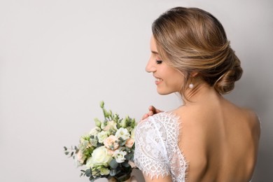 Young bride with elegant hairstyle holding wedding bouquet on beige background