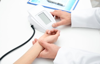 Photo of Doctor checking young woman's pulse and measuring blood pressure at table in hospital, closeup