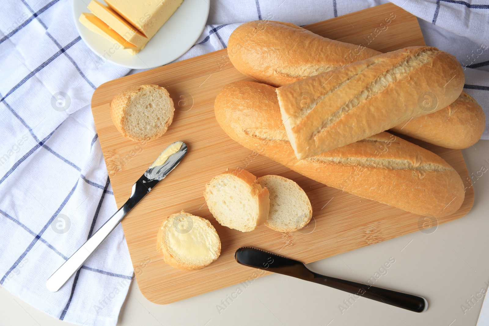 Photo of Tasty cut baguette with fresh butter on white table, flat lay