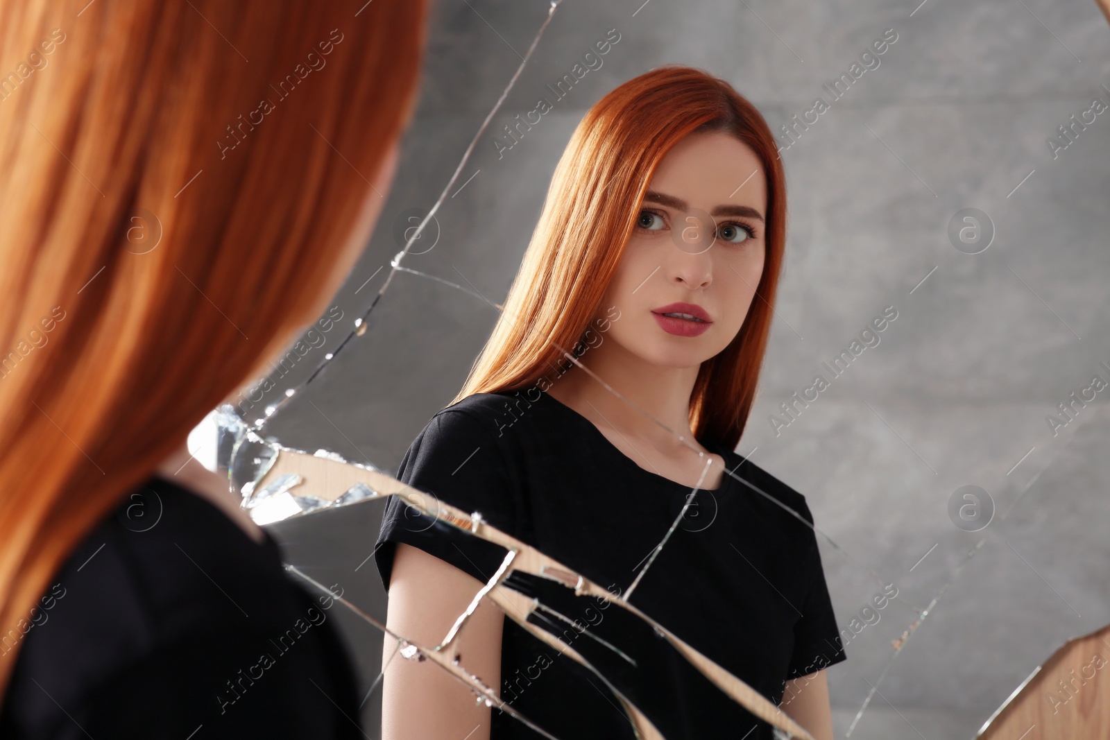 Photo of Mental problems. Depressed young woman looking at herself in broken mirror indoors