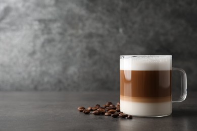 Photo of Hot coffee with milk in glass cup and beans on grey table. Space for text