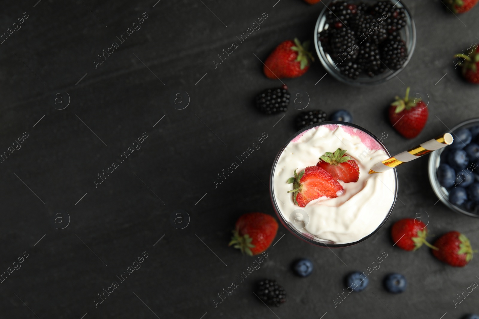 Photo of Tasty milk shake with whipped cream and fresh berries on black slate table, flat lay. Space for text