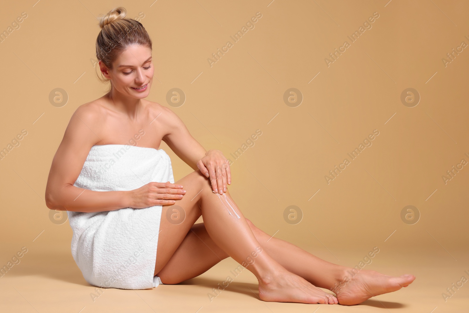 Photo of Woman applying body cream onto her leg against beige background, space for text