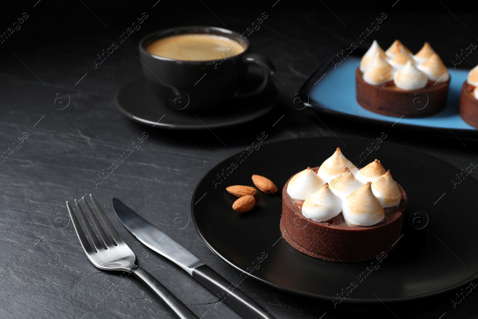 Photo of Delicious salted caramel chocolate tart with meringue and almonds on black table