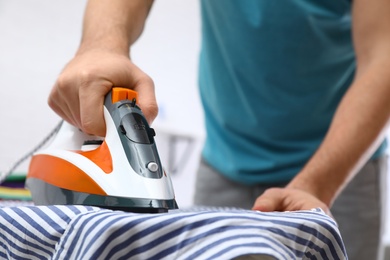 Photo of Man ironing shirt on board at home, closeup