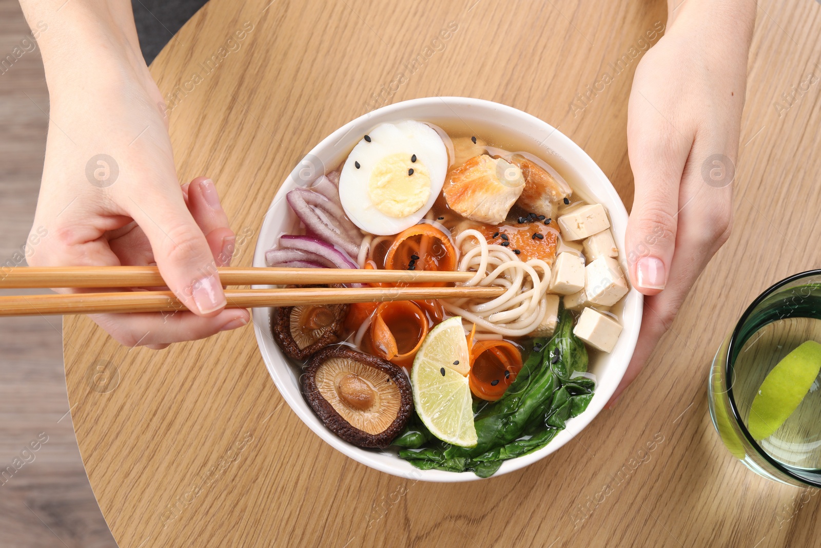 Photo of Woman eating delicious ramen with chopsticks at wooden table, top view. Noodle soup