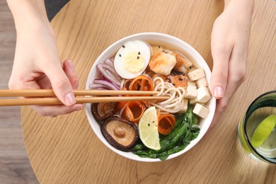 Photo of Woman eating delicious ramen with chopsticks at wooden table, top view. Noodle soup