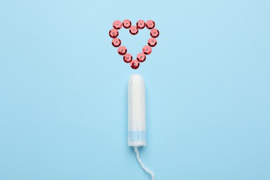 Tampon near heart made of red sequins on light blue background, flat lay. Menstrual hygiene product