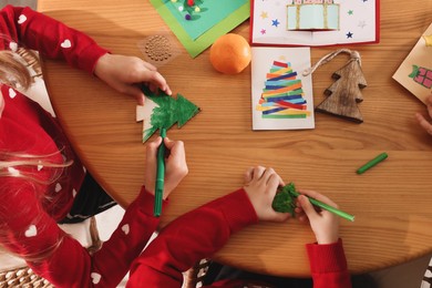 Photo of Little children making Christmas crafts at wooden table, top view