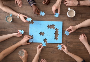 Photo of People with puzzle on wooden background, closeup of hands. Unity concept
