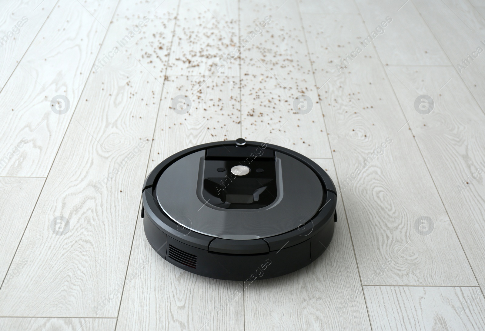 Photo of Modern robotic vacuum cleaner removing scattered buckwheat from wooden floor