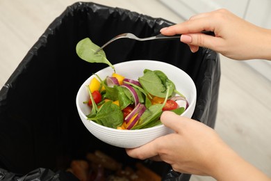 Photo of Woman throwing vegetable salad into bin indoors, closeup