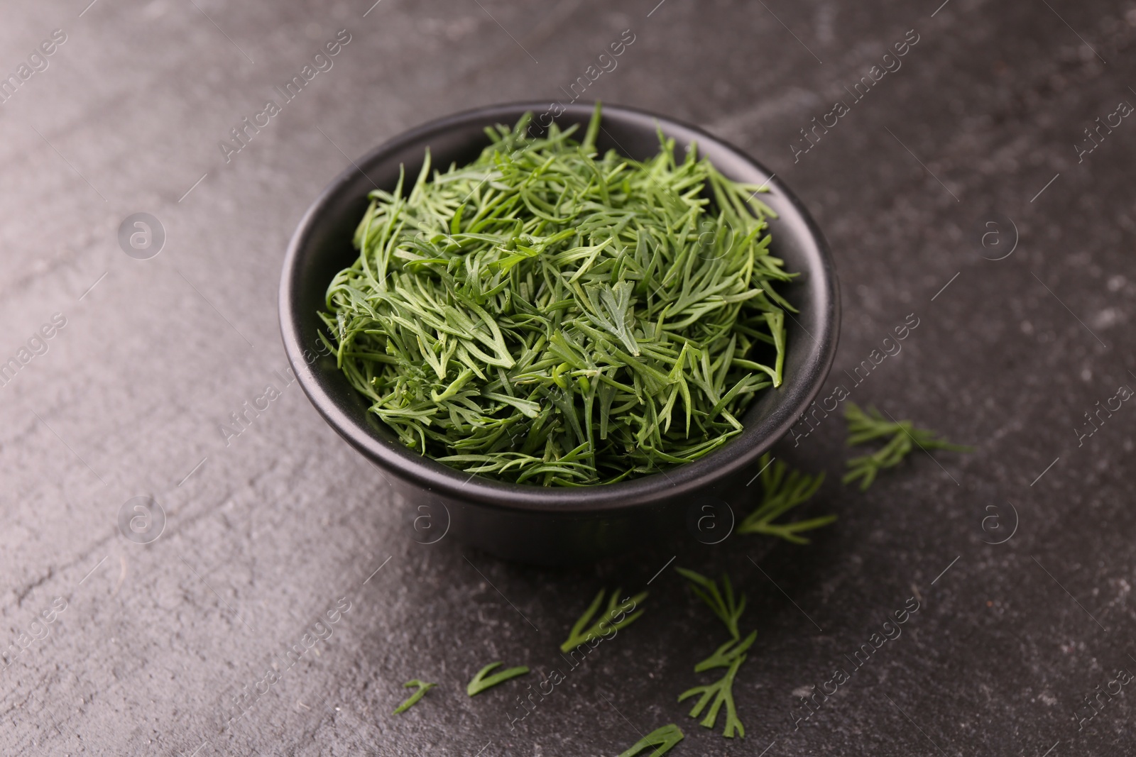 Photo of Fresh cut dill in bowl on dark textured table, closeup