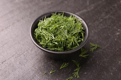 Fresh cut dill in bowl on dark textured table, closeup