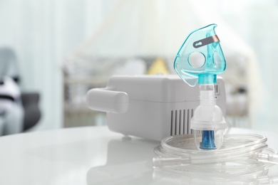 Photo of Modern nebulizer with face mask on white table in children's room. Equipment for inhalation