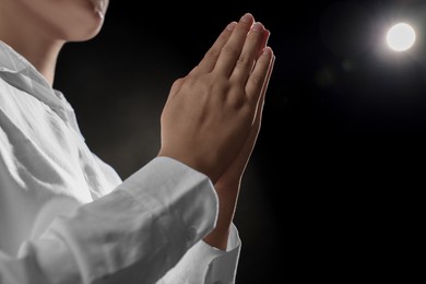 Photo of Woman holding hands clasped while praying on black background, closeup