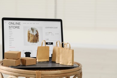 Photo of Online store. Laptop, small shopping bags and mini parcels on table indoors, space for text