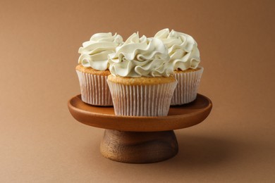 Photo of Tasty vanilla cupcakes with cream on dark beige background