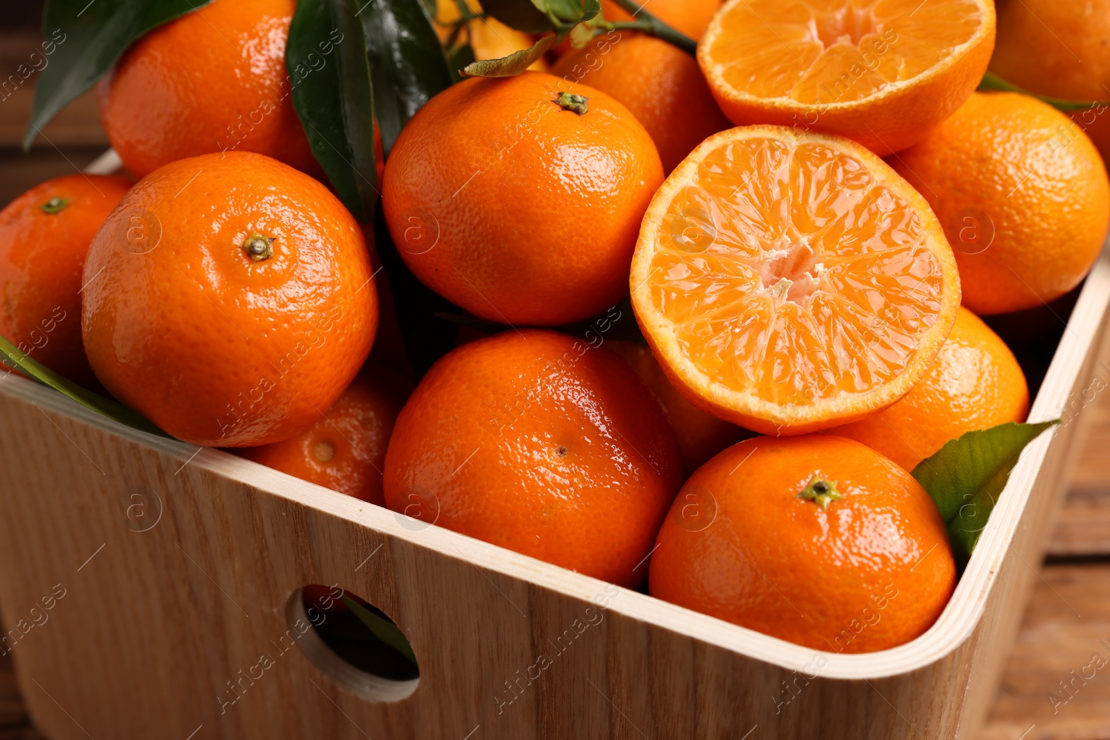 Photo of Fresh tangerines with green leaves in crate on wooden table, closeup