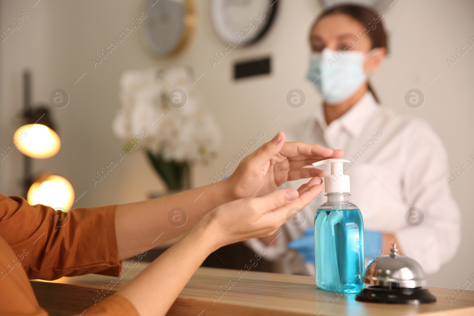 Photo of Woman applying antiseptic gel at hotel reception, closeup