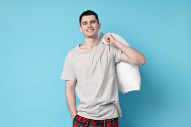 Happy man in pyjama holding pillow on light blue background