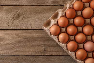 Photo of Fresh raw chicken eggs in carton on wooden table, top view. Space for text