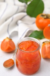 Jar of tasty persimmon jam and ingredients on white table, above view