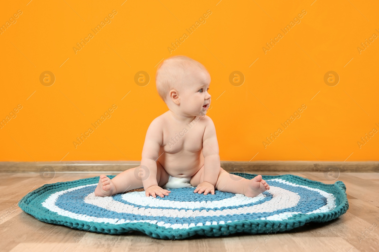 Photo of Cute little baby on soft rug near color wall