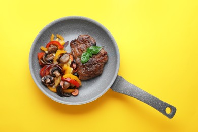 Tasty fried steak with vegetables in pan on yellow background, top view