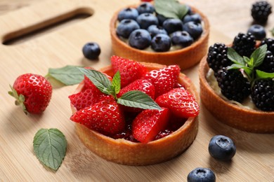 Tartlets with different fresh berries on wooden board, closeup. Delicious dessert