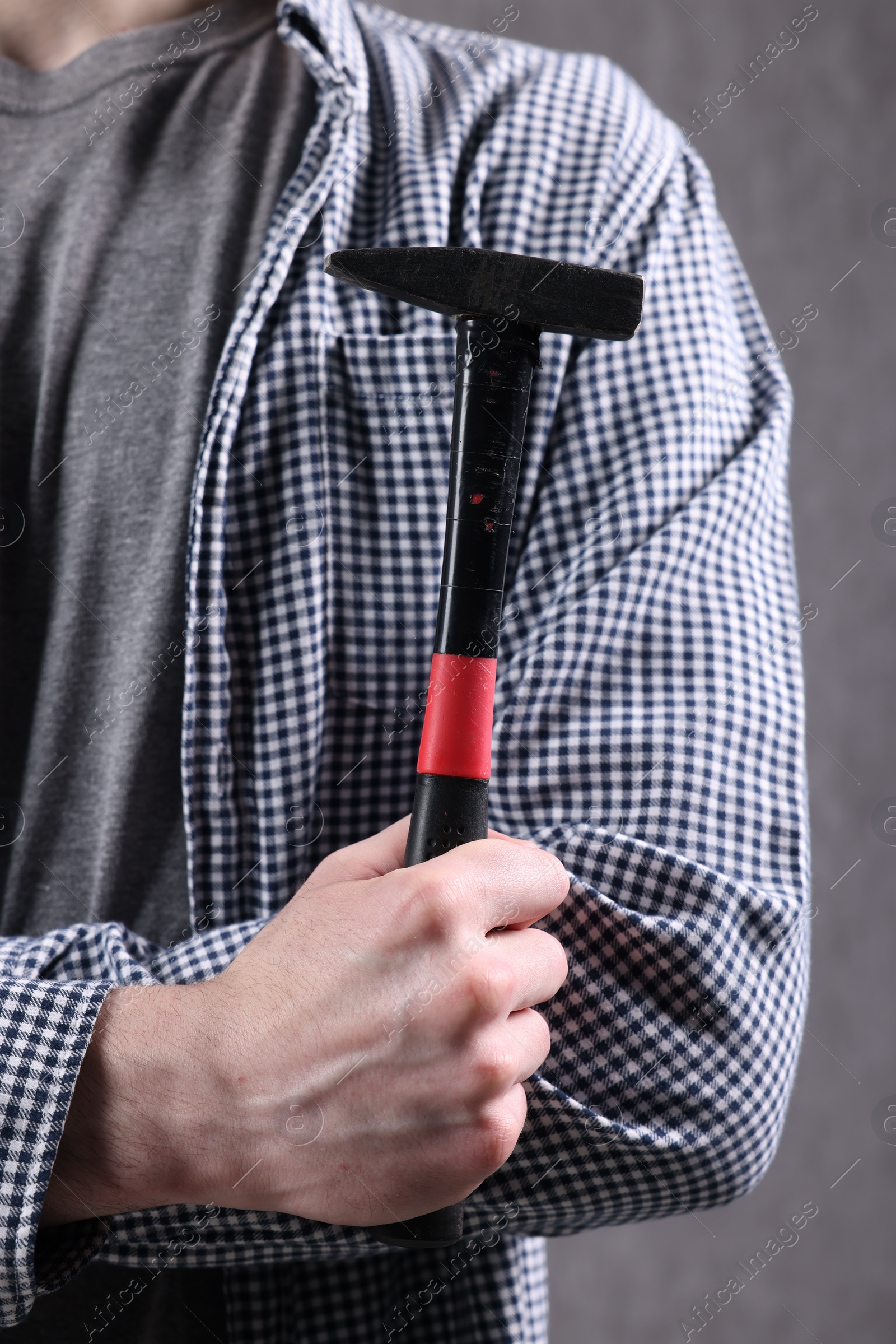 Photo of Young man holding hammer on grey background, closeup