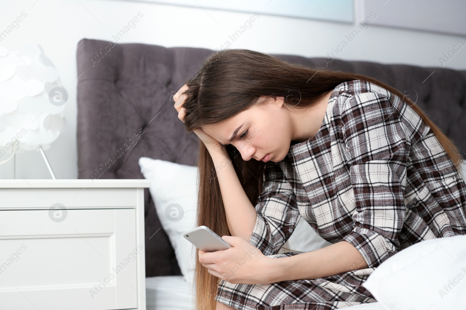 Photo of Upset teenage girl with smartphone sitting on bed. Space for text