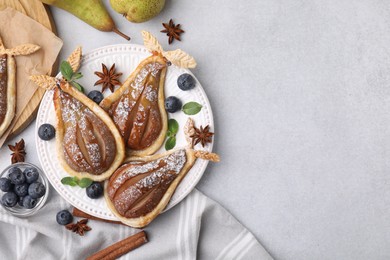 Delicious pears baked in puff pastry with powdered sugar served on light grey table, flat lay. Space for text