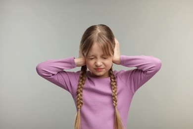 Photo of Hearing problem. Little girl suffering from ear pain on grey background