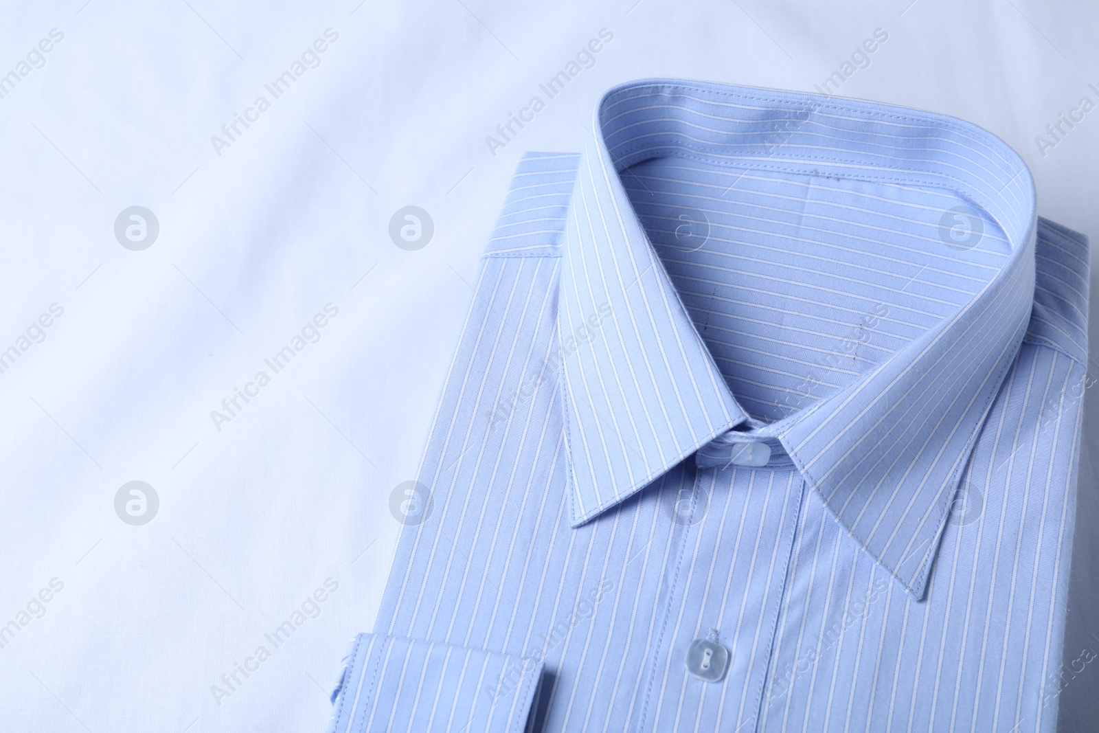 Photo of Stylish light blue shirt on white fabric, closeup. Dry-cleaning service