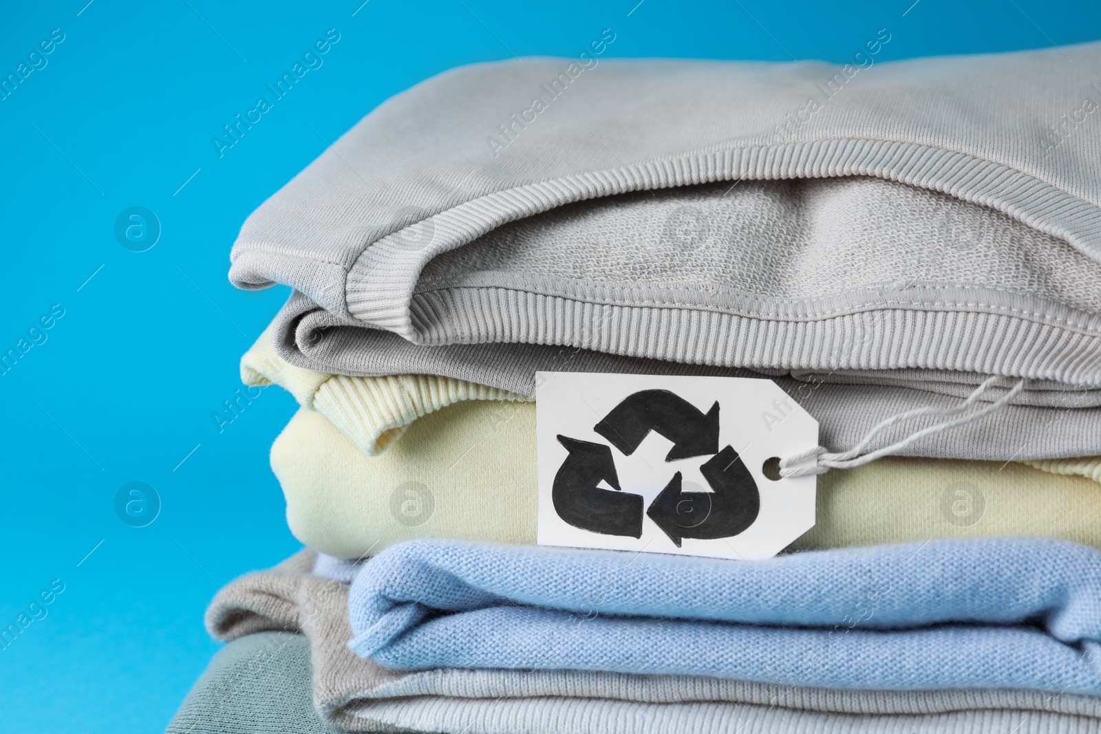 Photo of Stack of clothes with recycling label on light blue background, closeup