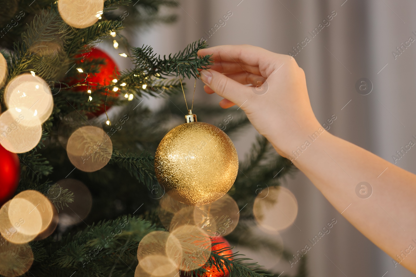 Photo of Woman decorating Christmas tree with golden festive ball on light background, closeup