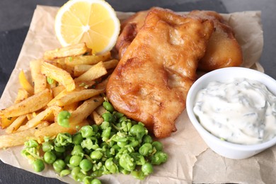 Photo of Tasty fish, chips, sauce and peas on table, closeup