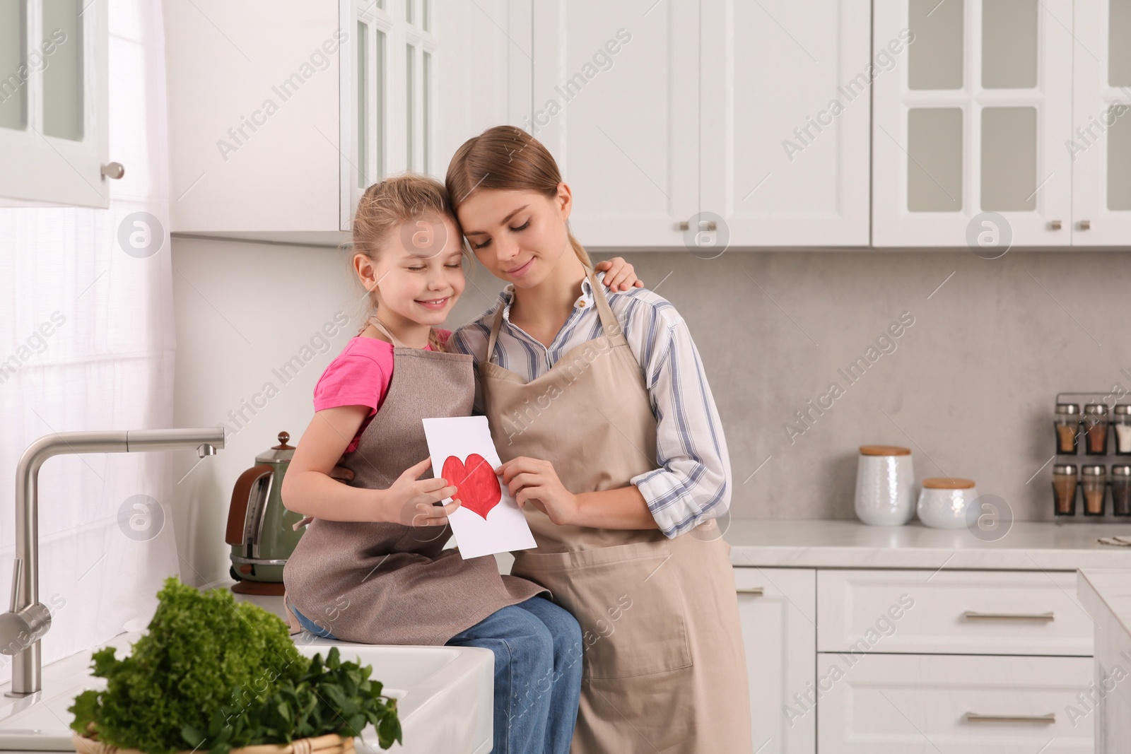 Photo of Little daughter congratulating mom with greeting card in kitchen. Happy Mother's Day