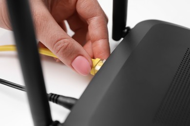 Photo of Woman connecting cable to router at white table, closeup. Wireless internet communication