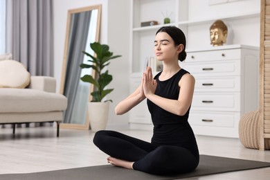 Beautiful girl meditating on yoga mat at home