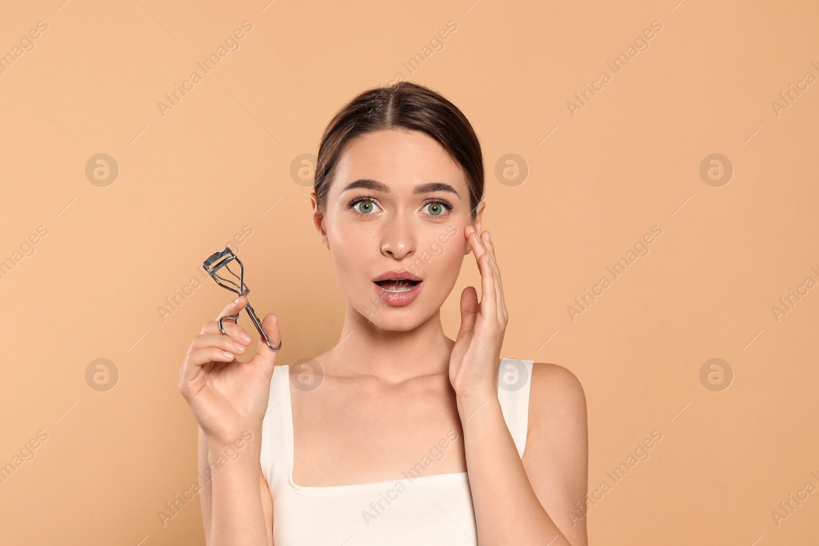 Photo of Emotional woman with eyelash curler on beige background