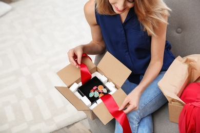 Young woman opening parcel on sofa in living room