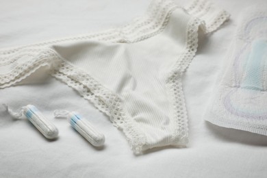 Photo of Woman's panties, menstrual pad and tampons on white fabric
