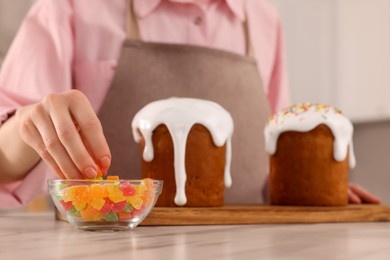 Woman decorating delicious Easter cake with pieces of candied fruits at white marble table in kitchen, closeup