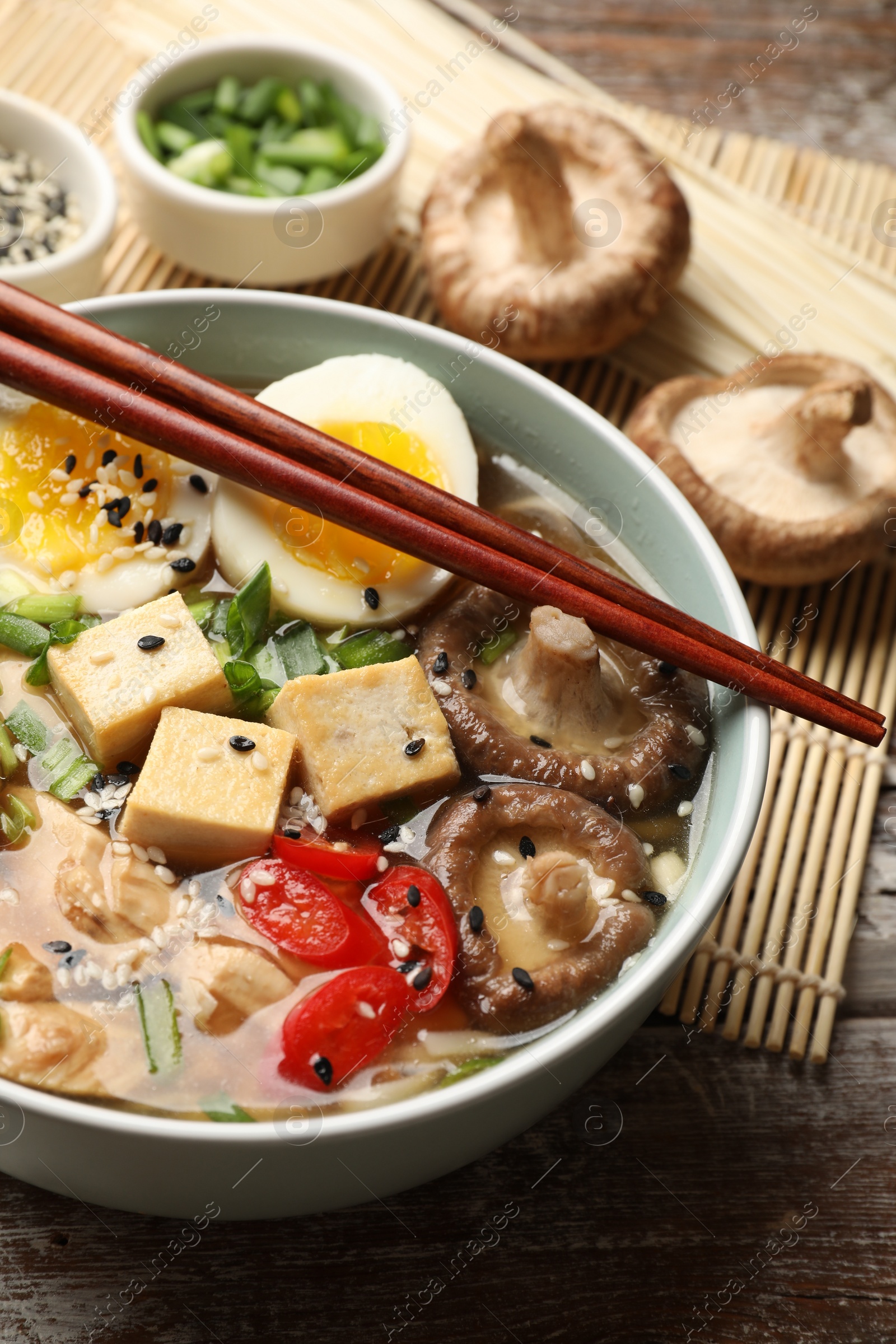 Photo of Noodle soup. Bowl of delicious ramen and chopsticks on wooden table, closeup