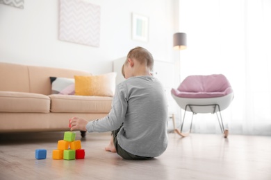 Photo of Lonely little boy playing with cubes on floor at home. Autism concept