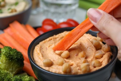 Woman dipping carrot stick into hummus at table, closeup