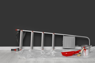 Photo of Metallic folding ladder and painting tools near gray wall indoors, space for text