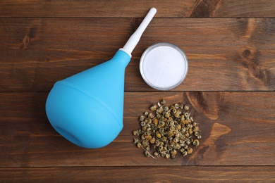 Medical enema, soda powder and dry chamomile flowers on wooden background, flat lay